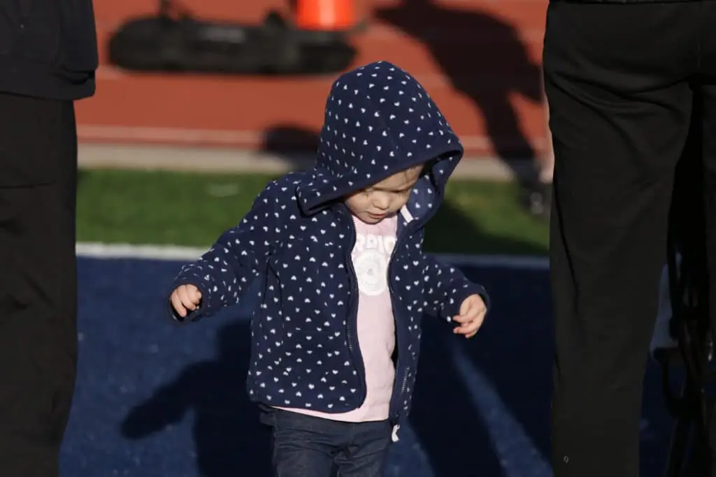 Toddler in a navy fleece walking the Kids Fun Run on the field at the Hustle for Heroes 5K