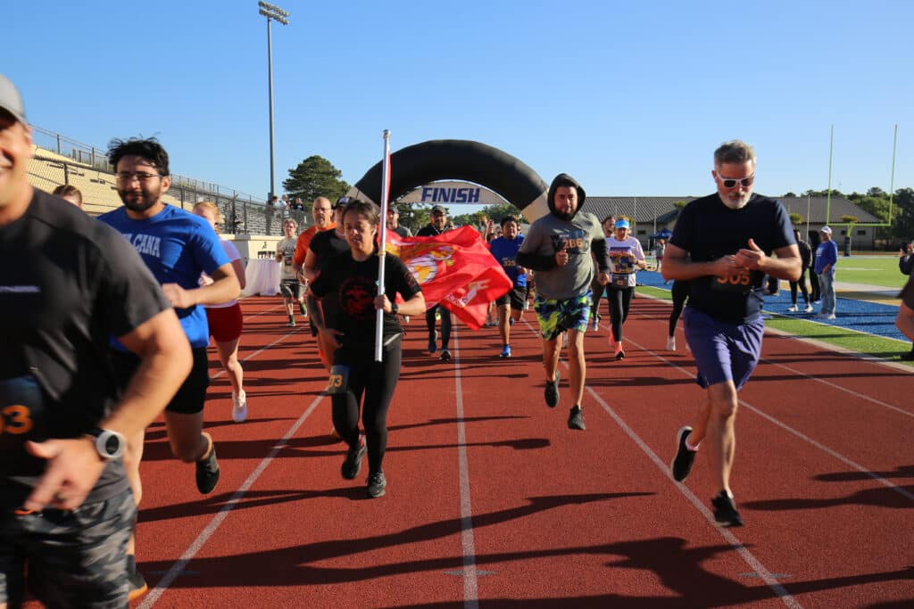The Hustle for Heroes 5K field takes off from the start on the track at Charleston Southern University, with a participant carrying the Marine Corps flag