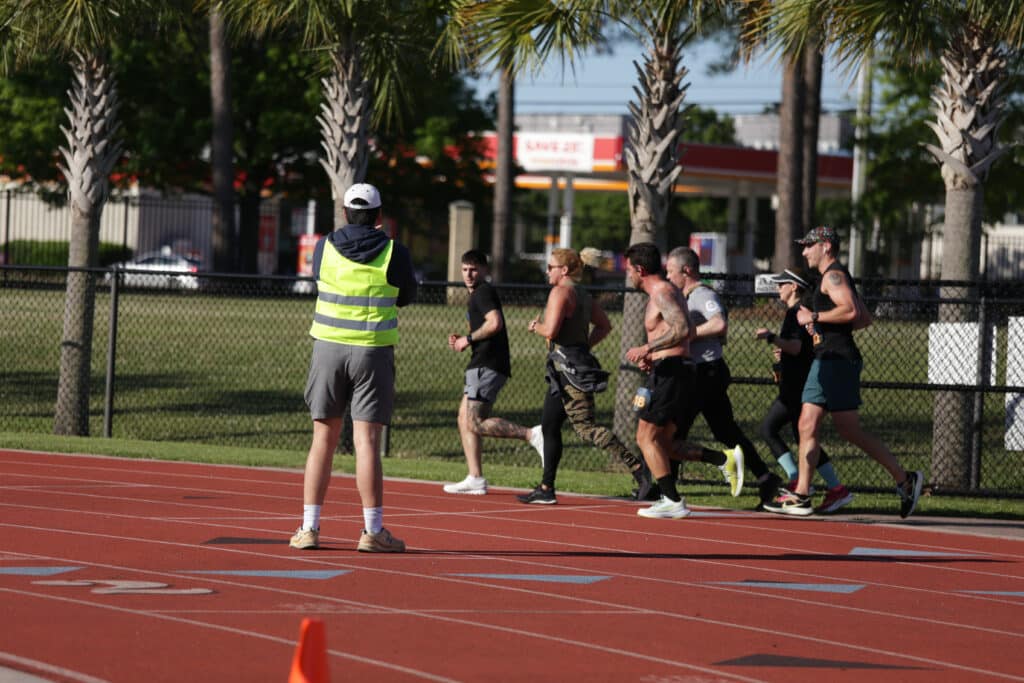 A volunteer in a yellow safety vest watches Hustle for Heroes 5K runners pass on the track at Charleston Southern University