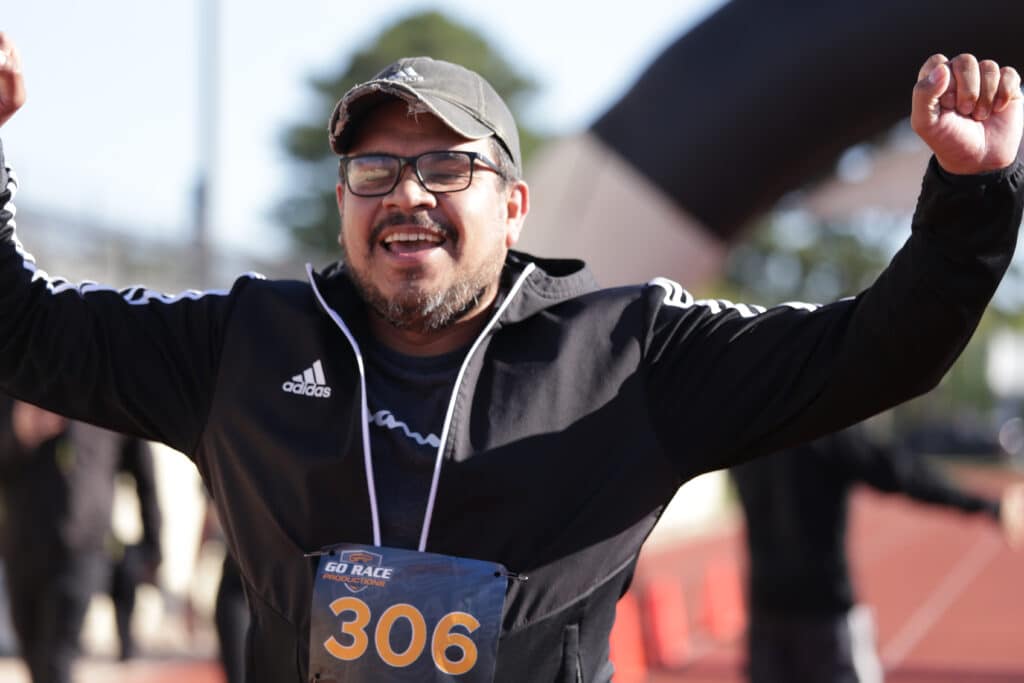 Hustle for Heroes 5K participant raising both arms and smiling as he crosses the finish line