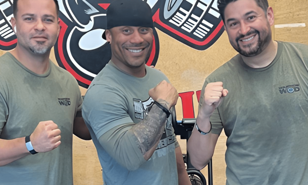 Three post-9/11 combat veterans in WarriorWOD gear after a workout session, smiling and raising fists — participants in WarriorWOD Foundation's six-month PTSD recovery program.