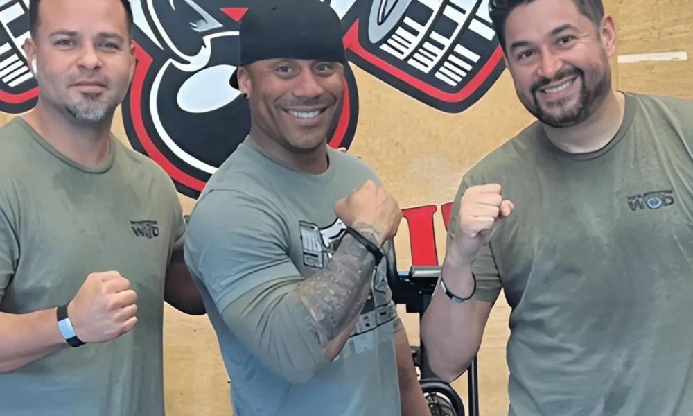 Three post-9/11 combat veterans in WarriorWOD gear after a workout session, smiling and raising fists — participants in WarriorWOD Foundation's six-month PTSD recovery program.