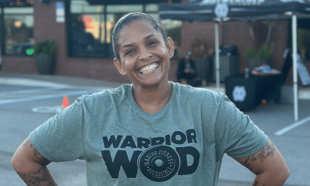 Smiling woman veteran in a WarriorWOD t-shirt standing with hands on hips outside a gym